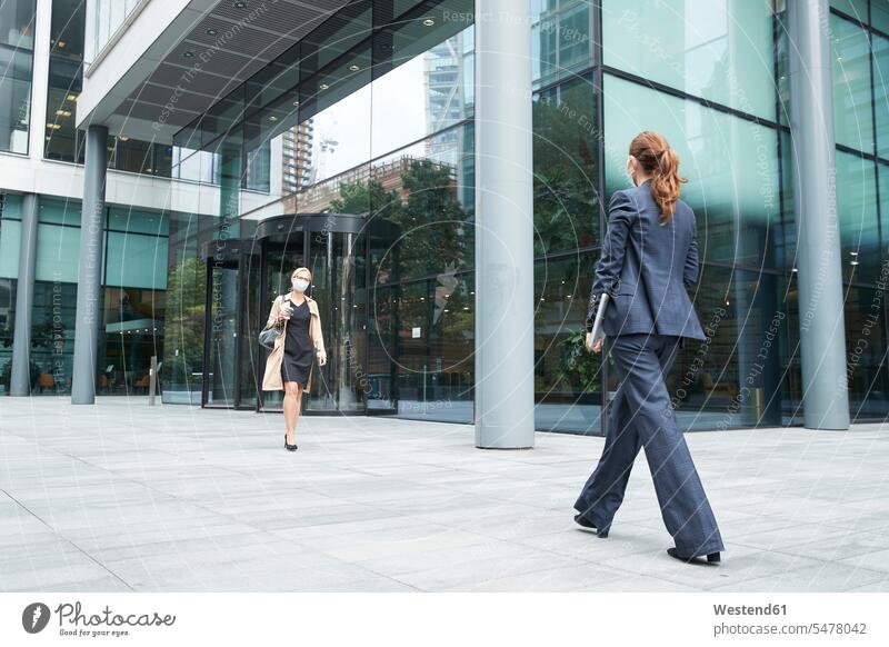 Business people wearing face mask while walking against office building color image colour image outdoors location shots outdoor shot outdoor shots day