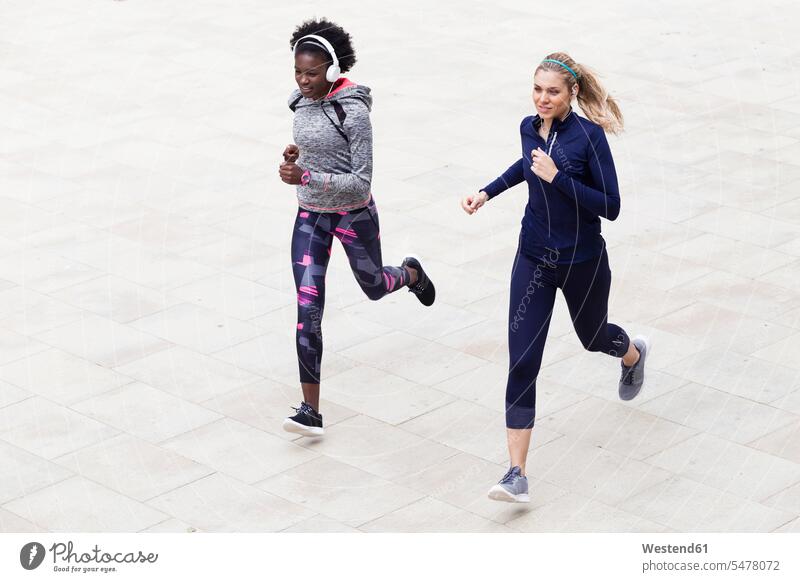 Two sporty young women running together in the city town cities towns sportive sporting athletic woman females Jogging female friends outdoors outdoor shots