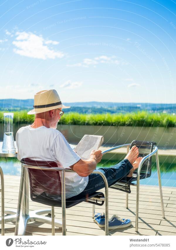 Rear view of senior man reading newspapper, sitting at swimming pool Seated chair chairs newspaper newspapers vacation Holidays pools swimming pools senior men