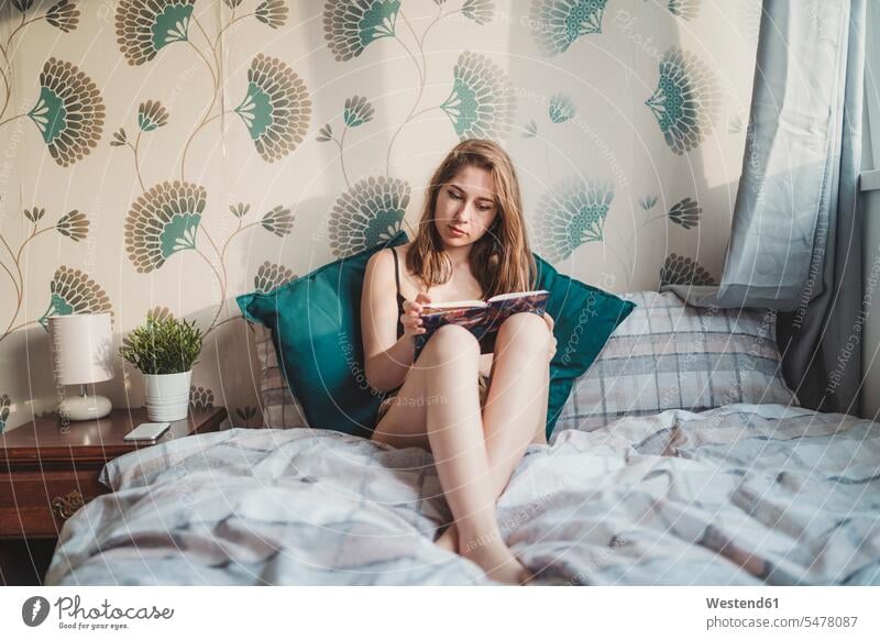 Attractive young woman sitting in bed at home with book human human being human beings humans person persons celibate celibates singles solitary people