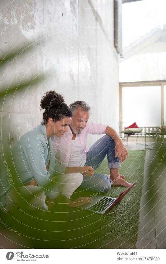 Casual businessman and businesswoman sitting on artificial turf in a loft sharing laptop Laptop Computers laptops notebook casual Businessman Business man