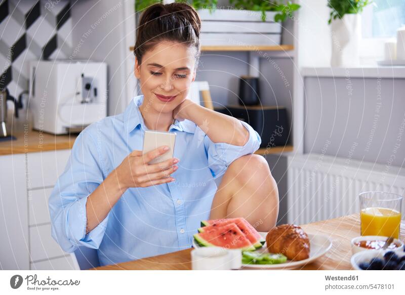 Young woman at home in kitchen, using smartphone morning in the morning Smartphone iPhone Smartphones domestic kitchen kitchens use Fruit Fruits young women