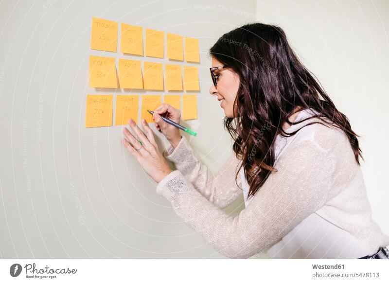 Young woman standing in office at a wall taking notes on adhesive notes human human being human beings humans person persons caucasian appearance