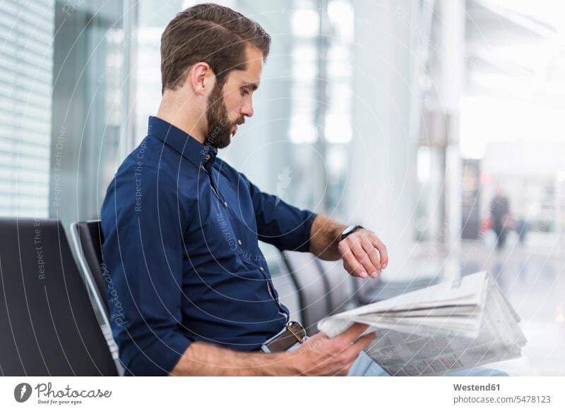 Young businessman sitting in waiting area checking the time wrist watch Wristwatch Wristwatches wrist watches Time Seated Businessman Business man Businessmen