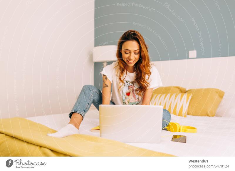 Young woman using laptop on bed at home human human being human beings humans person persons celibate celibates singles solitary people solitary person pants