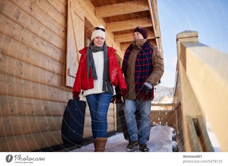 Mature couple with suitcases walking at mountain hut in winter twosomes partnership couples going mountain shelter alpine hut mountain huts mountain lodge