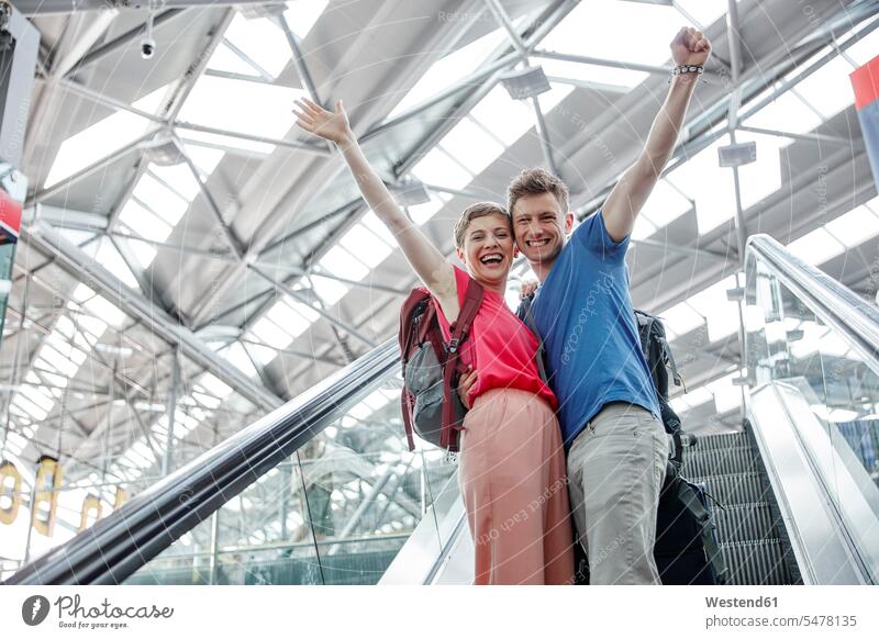 Happy couple cheering on escalator at the airport jubilation happiness happy terminal airports moving staircase moving stairs Escalators twosomes partnership