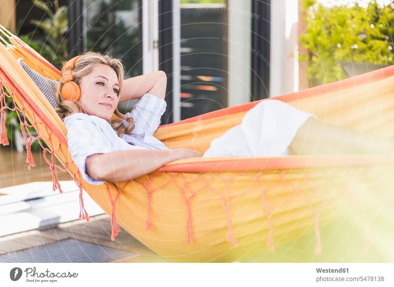 Portrait of pensive mature woman lying in hammock on terrace listening music with headphones hammocks headset relax relaxing hear contemplative pensively