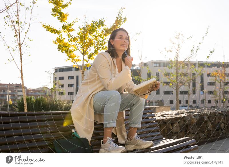 Thoughtful businesswoman sitting on bench with book color image colour image outdoors location shots outdoor shot outdoor shots day daylight shot daylight shots