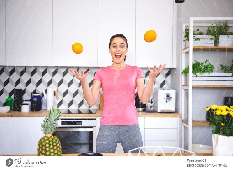 Portrait of young woman juggling with oranges in the kitchen portrait portraits juggle domestic kitchen kitchens females women Orange Citrus sinensis Oranges
