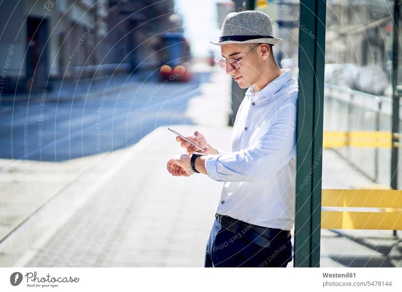 Young man checking time at a tram stop in the city Mixed Race Person mixed-race Person mixed race ethnicity fashionable date appointment wireless