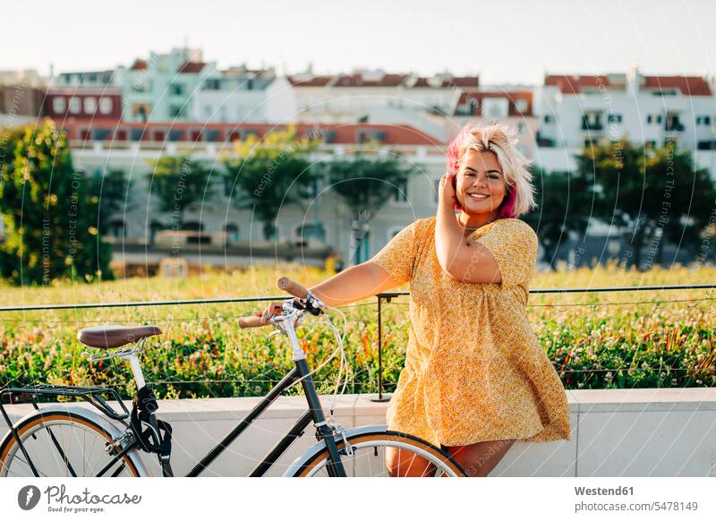 Happy plus size woman with bicycle leaning on park fence color image colour image outdoors location shots outdoor shot outdoor shots day daylight shot
