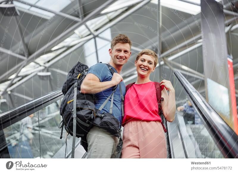 Happy couple on escalator at the airport twosomes partnership couples moving staircase moving stairs Escalators terminal airports happiness happy people persons