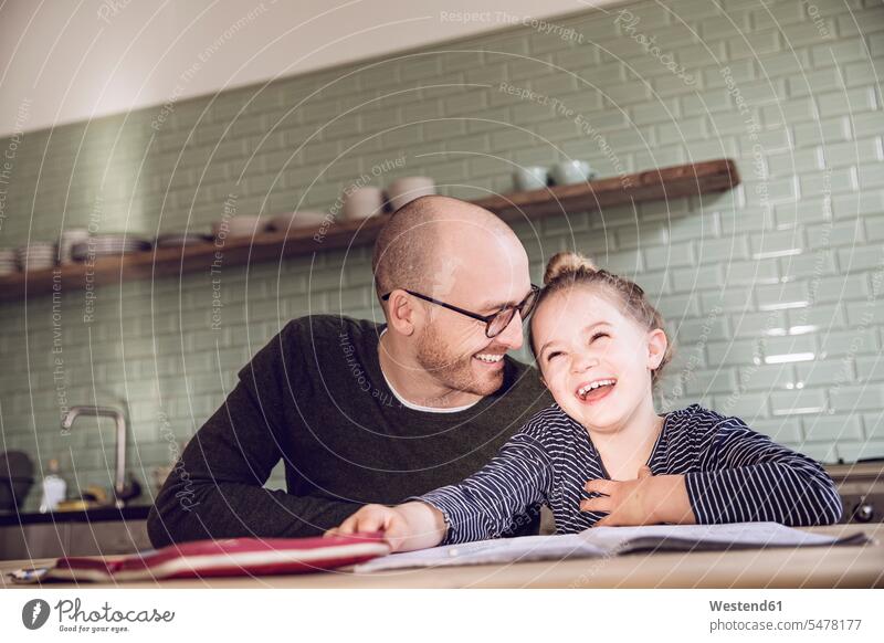 Father and daughter sitting in kitchen, doing homework learning Seated daughters father pa fathers daddy dads papa Home work child children family families