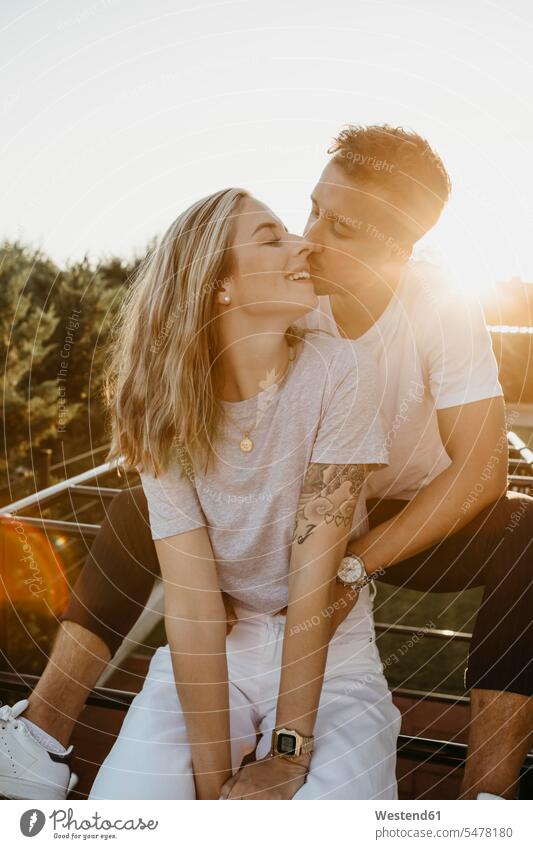 Young couple kissing each other on a climbing frame at sunset smile Seated sit embrace Embracement hug hugging in the evening delight enjoyment Pleasant