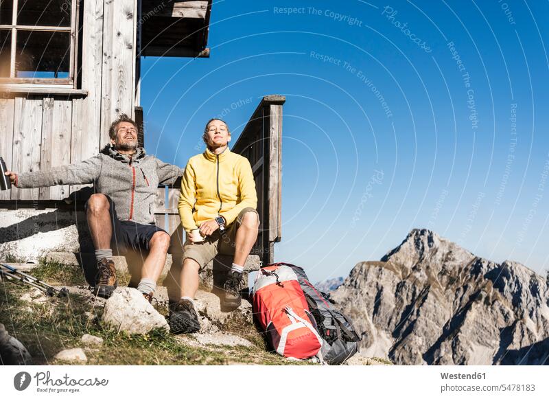 Hiking couple sitting in front of mountain hut, taking a break resting mountain range mountains mountain ranges mountain shelter alpine hut mountain huts