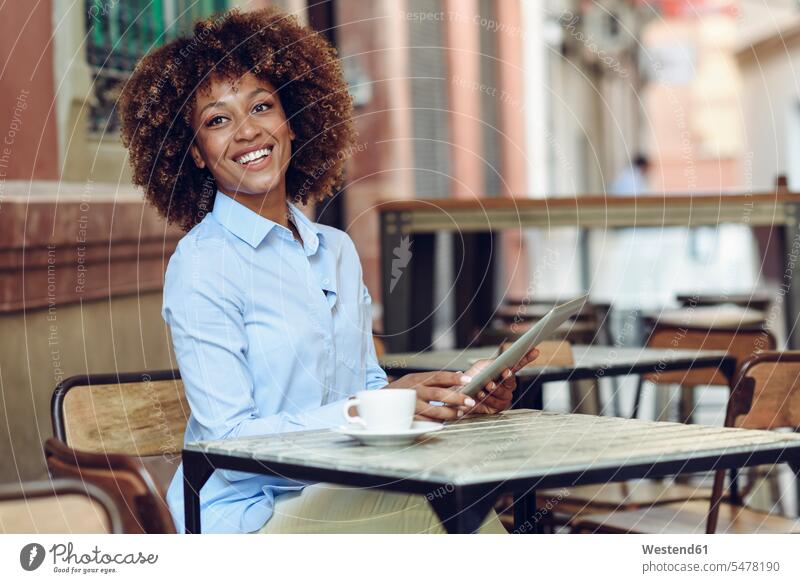 Smiling woman with afro hairstyle sitting in outdoor cafe with tablet females women Afro Afros digitizer Tablet Computer Tablet PC Tablet Computers iPad