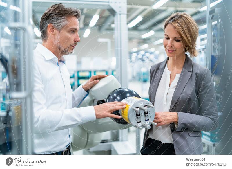 Businesswoman and man talking at assembly robot in a factory human human being human beings humans person persons caucasian appearance caucasian ethnicity
