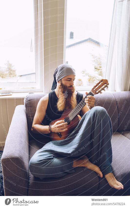 Bearded man playing guitar on couch sitting Seated men males beard settee sofa sofas couches settees guitars Adults grown-ups grownups adult people persons