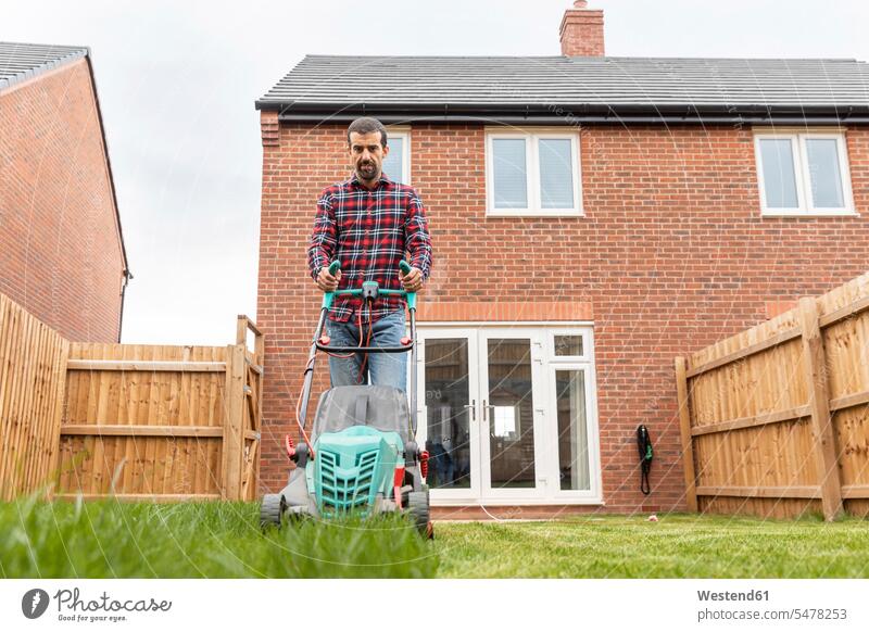 Mid adult man using lawn mower for mowing at backyard color image colour image outdoors location shots outdoor shot outdoor shots day daylight shot