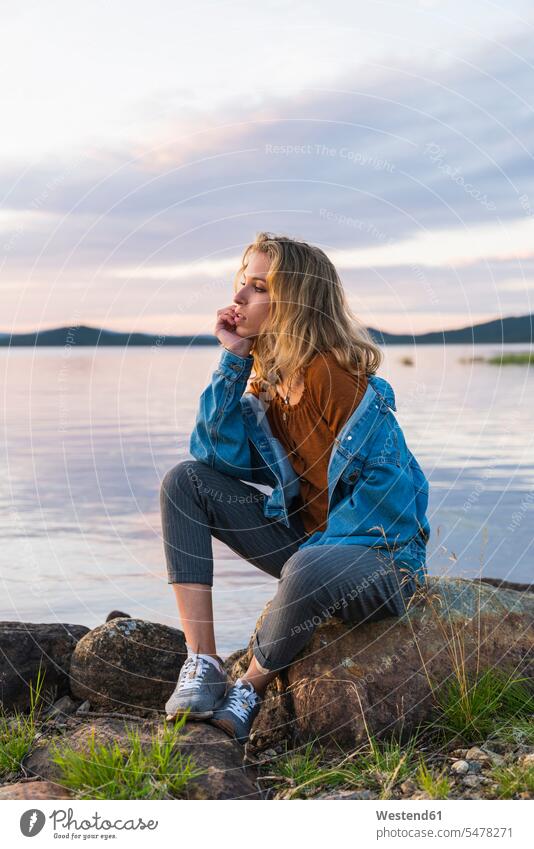 Finland, Lapland, young woman sitting on a rock at the lakeside rocks landscape landscapes scenery terrain females women Seated water waters body of water
