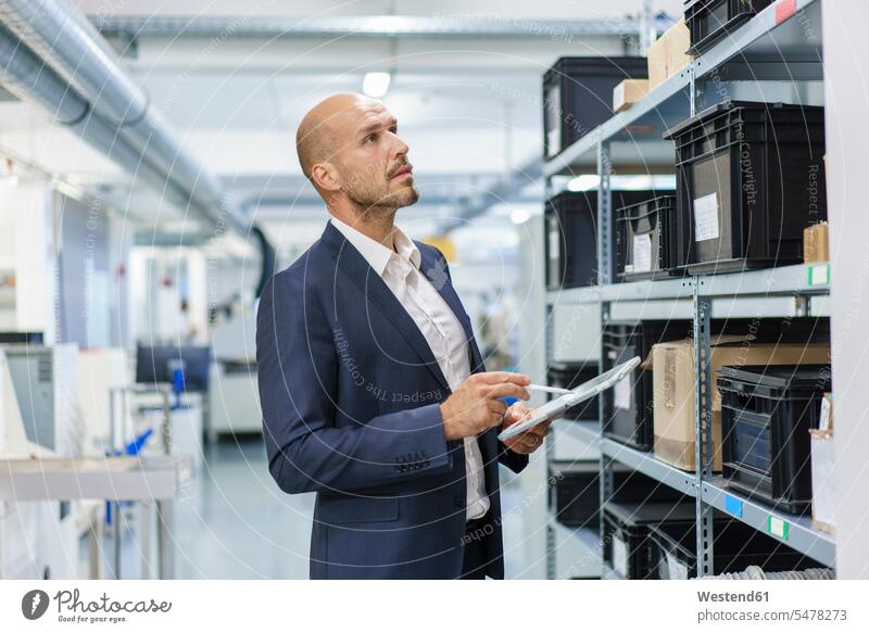 Mature male professional with digital tablet looking at containers on rack in industry color image colour image indoors indoor shot indoor shots interior