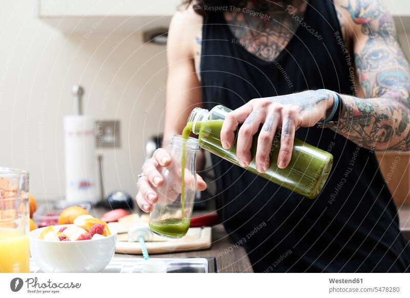 Tattooed young man pouring in healthy smoothie in kitchen tattooed Smoothies men males tattoos Drink beverages Drinks Beverage food and drink Nutrition