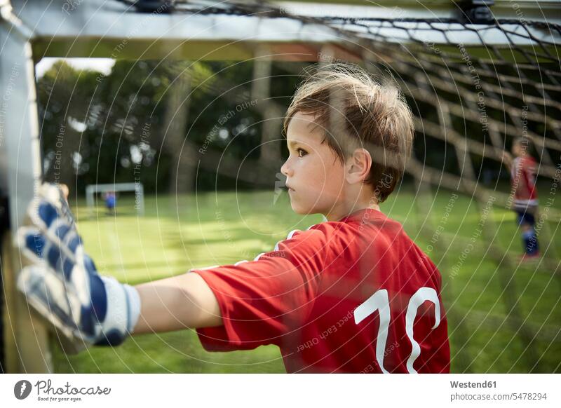 Serious boy in soccer uniform holding goal post at field color image colour image outdoors location shots outdoor shot outdoor shots day daylight shot