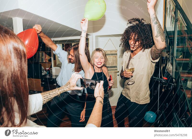 Woman photographing happy friends dancing during social gathering at home color image colour image indoors indoor shot indoor shots interior interior view