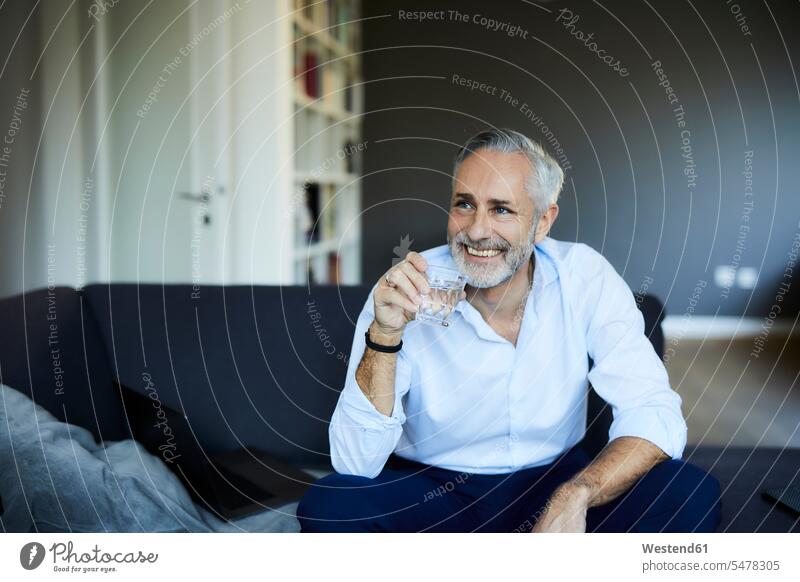 Smiling mature man drinking glass of water on the sofa at home human human being human beings humans person persons celibate celibates singles solitary people