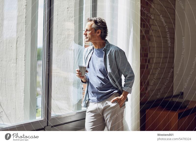 Senior man looking out of window in a loft flat windows relax relaxing relaxation clear fair light stand interior equipment free time leisure time Distinct