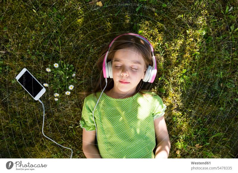 Girl lying on meadow listening music with headphones and smartphone hearing portrait portraits Smartphone iPhone Smartphones laying down lie lying down meadows
