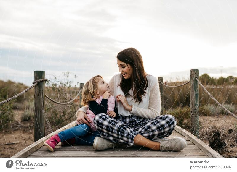 Happy mother and daughter sitting on a boardwalk in the countryside relax relaxing smile Seated play delight enjoyment Pleasant pleasure Cheerfulness