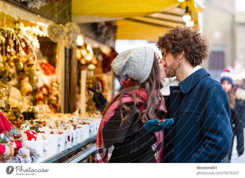 Happy affectionate young couple kissing at Christmas market Affection Affectionate happiness happy twosomes partnership couples kisses Event Events people