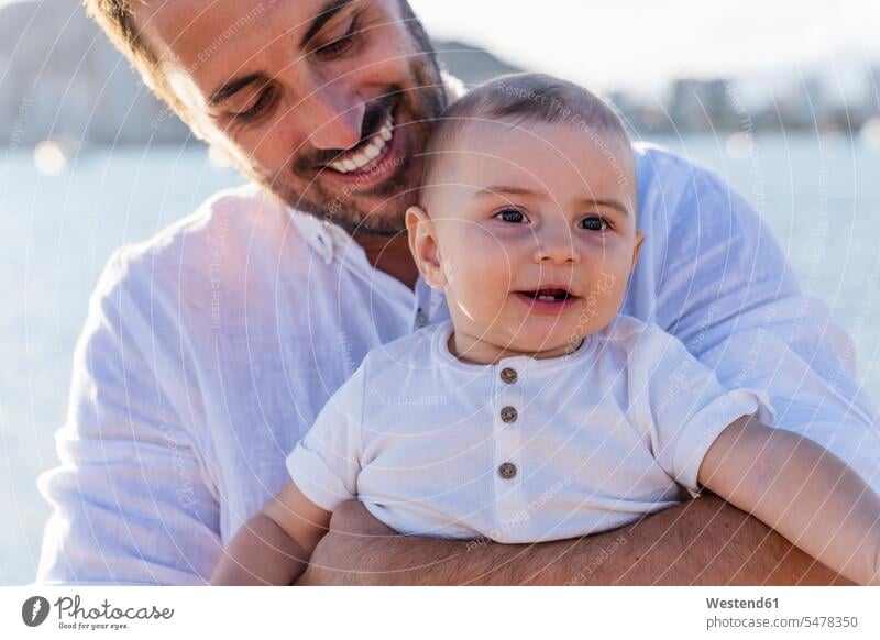 Close-up of smiling father carrying cute son at beach during sunset color image colour image Spain leisure activity leisure activities free time leisure time
