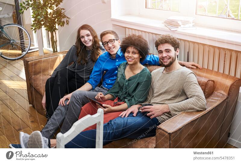 Portrait of smiling young people sitting on sofa with tablet smile portrait portraits couch settee sofas couches settees Seated digitizer Tablet Computer