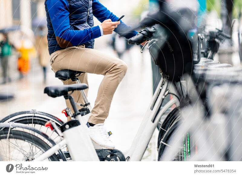 Man using smart phone sitting on electric bicycle at parking station during coronavirus color image colour image outdoors location shots outdoor shot
