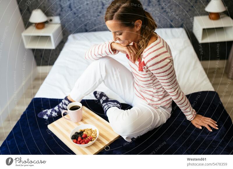 Smiling woman looking at food and coffee while sitting on bed at home color image colour image indoors indoor shot indoor shots interior interior view Interiors