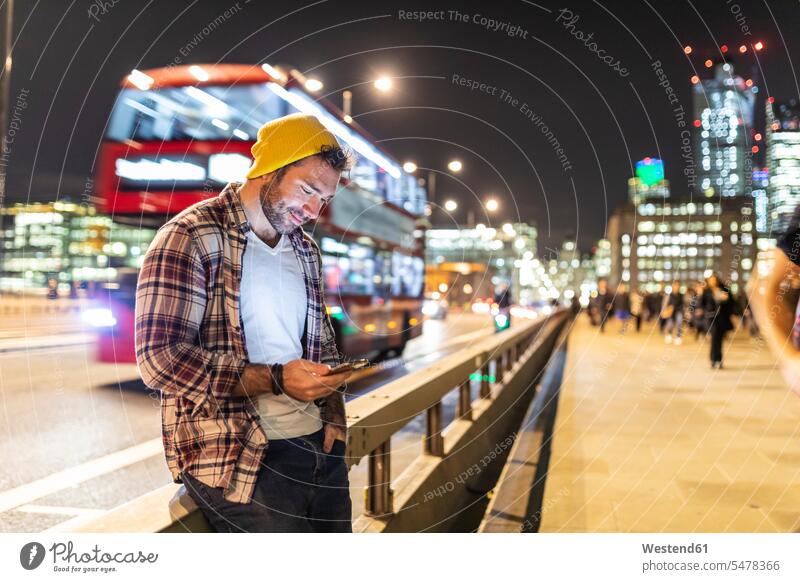 UK, London, smiling man using phone at the street in the city at night by night nite night photography town cities towns mobile phone mobiles mobile phones