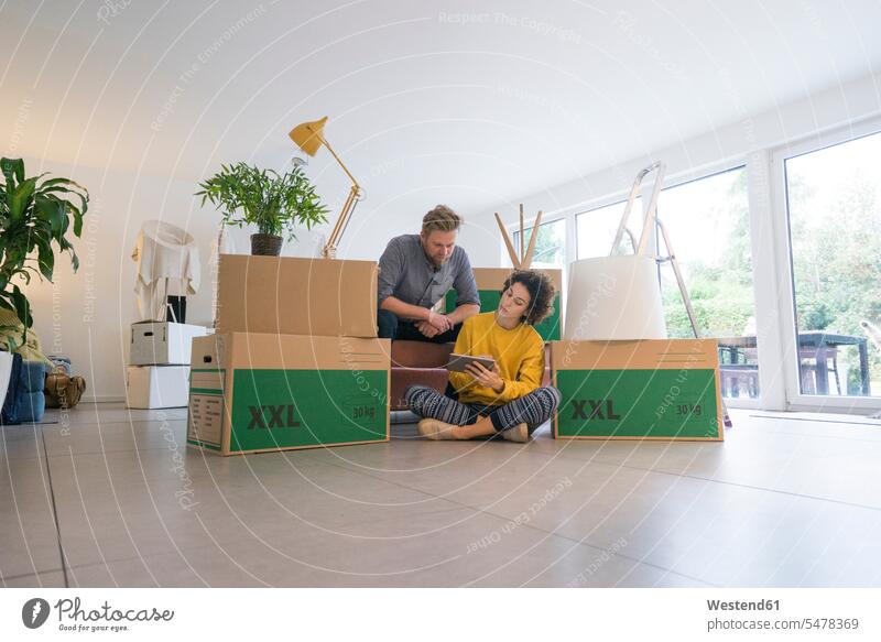 Couple sitting in living room with cardboard boxes using tablet couple twosomes partnership couples digitizer Tablet Computer Tablet PC Tablet Computers iPad