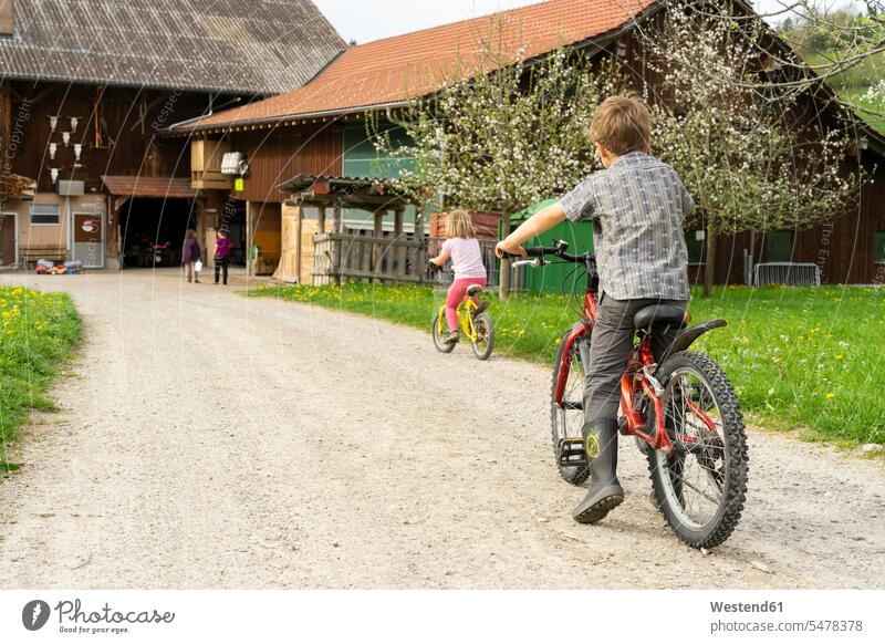 Girl and boy riding bicycle at a farm bikes cycles bicycles modesty country countryside free time leisure time roads street streets paths track tracks trail