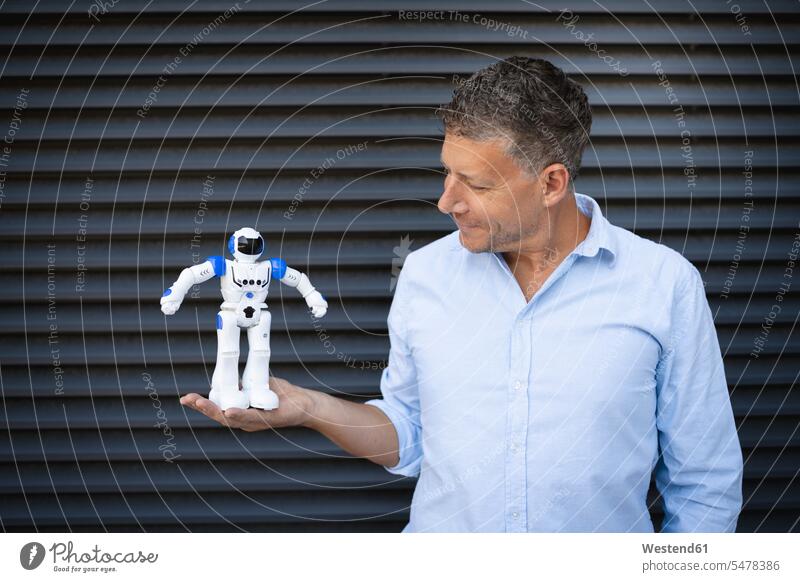 Businessman holding robot while standing against metal wall color image colour image outdoors location shots outdoor shot outdoor shots day daylight shot