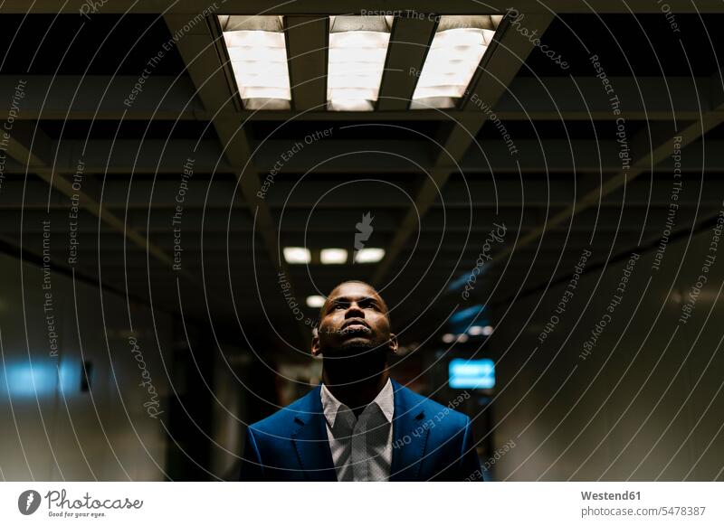 Male entrepreneur looking up while standing under illuminated light in subway color image colour image Spain Businessman Businessmen Business man Business men