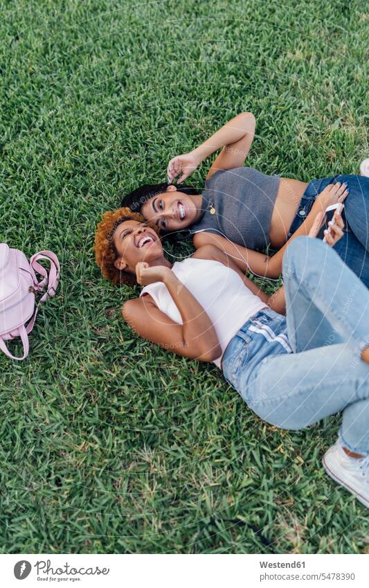 Two happy female friends relaxing in a park listening to music hearing happiness relaxed relaxation parks mate friendship leisure free time leisure time beauty