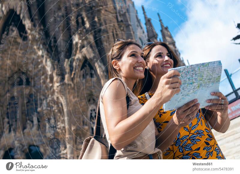 Smiling friends using map while standing against Sagrada Familia at Barcelona, Catalonia, Spain color image colour image outdoors location shots outdoor shot