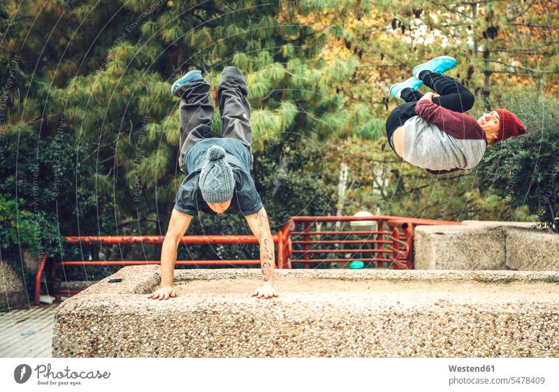Young man performing handstand while friend jumping in park autumn fall season seasons casual clothing casual wear leisure wear casual clothes Casual Attire