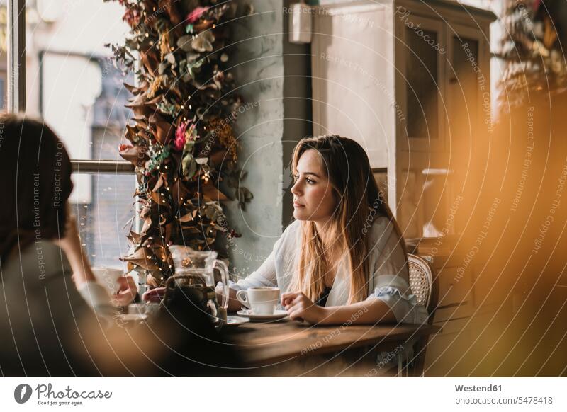 Two young women sitting at table in a cafe female friends thinking decorated daydreaming dreamy Contemplation reflection Contemplating contemplate Coffee Cup