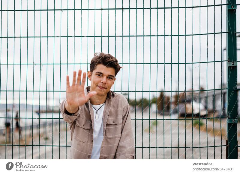 Handsome young man showing hand against metallic fence color image colour image Portugal outdoors location shots outdoor shot outdoor shots day daylight shot