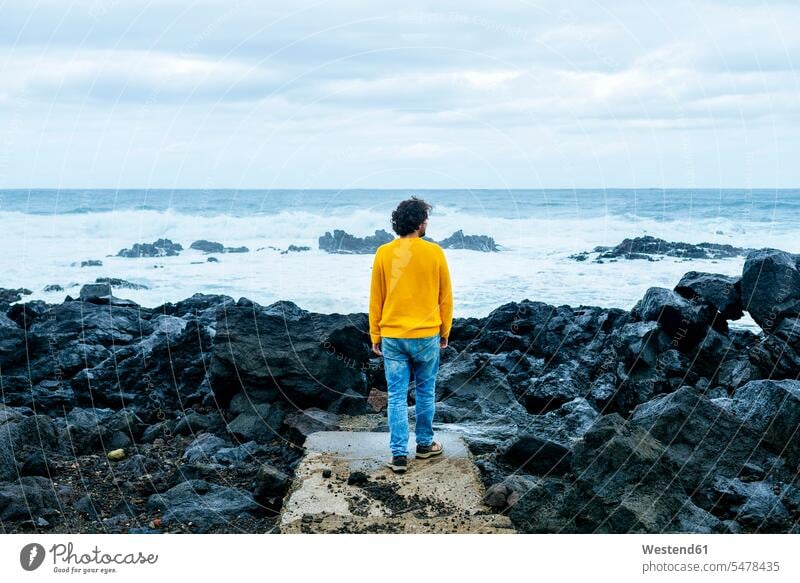 Azores, Sao Miguel, rear view of man looking at the sea from stony coast men males ocean standing coastline shoreline seeing viewing Adults grown-ups grownups
