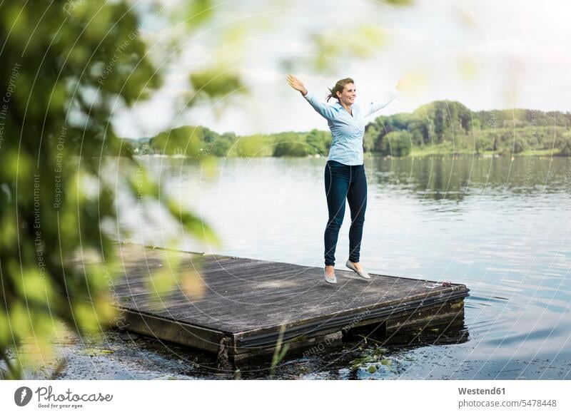 Woman doing a jumping jack on jetty at a lake jetties lakes woman females women water waters body of water Adults grown-ups grownups adult people persons